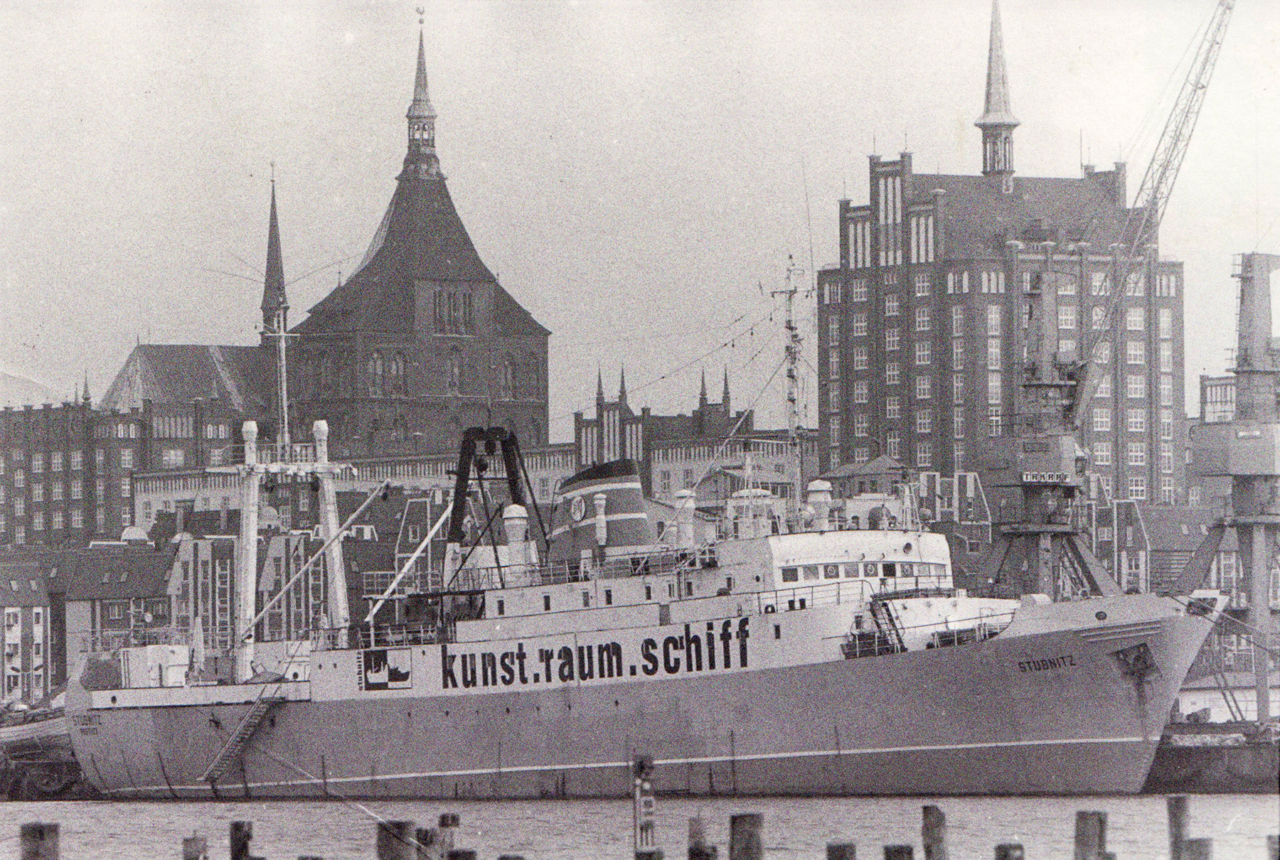 Stubnitz in Rostock 1993. Aufschrift auf der Schiffsseite "kunst.raum.schiff". Im Hintergrund Backsteingebäude.