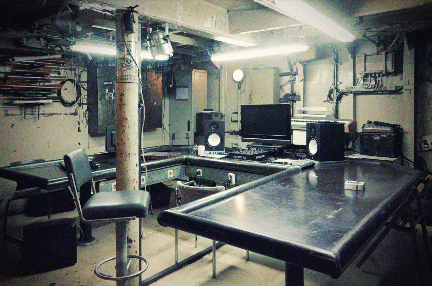 Der Arbeitsbereich im Audio Video Lab. Ein großer Tisch in U-Form auf dem ein Bildschirm und große Lautsprecher stehen. 
