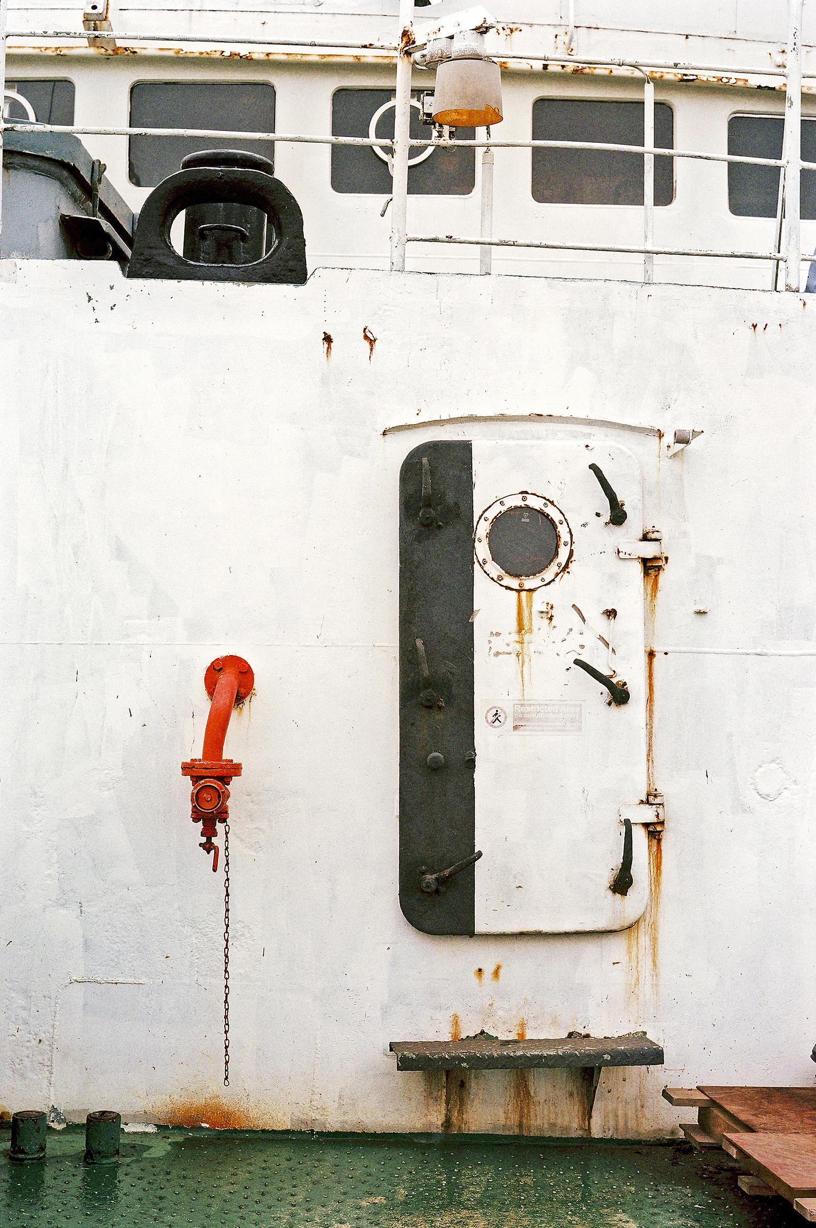 Schwarz-weißer Schott (Schiffstür) auf dem Brückendeck mit einigen Rostflecken. An der weißen Wand daneben befindet sich ein rot lackiertes Rohr.