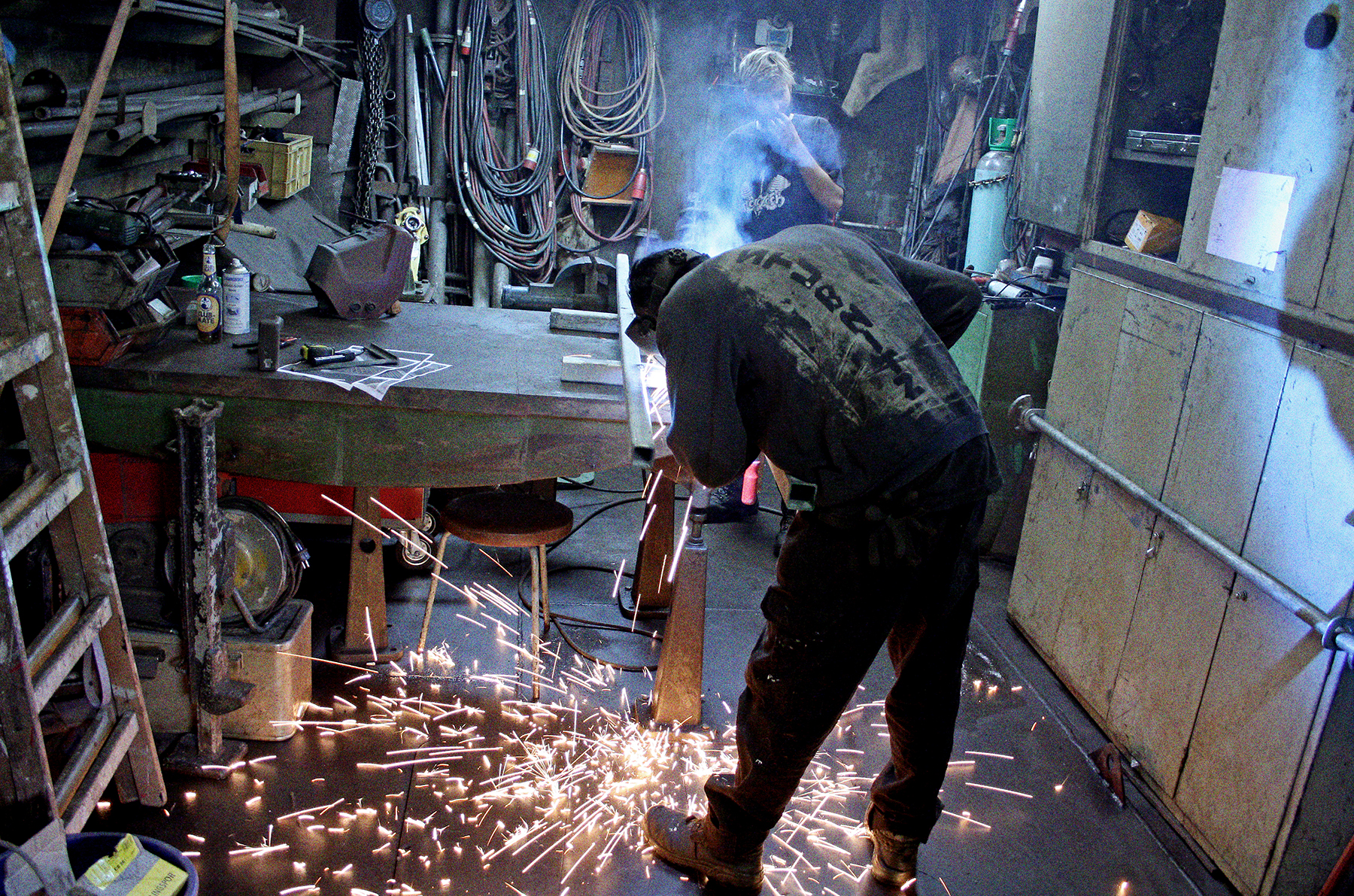 Arbeiten in der Metallwerkstatt. Ein Mensch bearbeitet ein Metallstück mit einem Winkelschleifer. Funken sprühen.