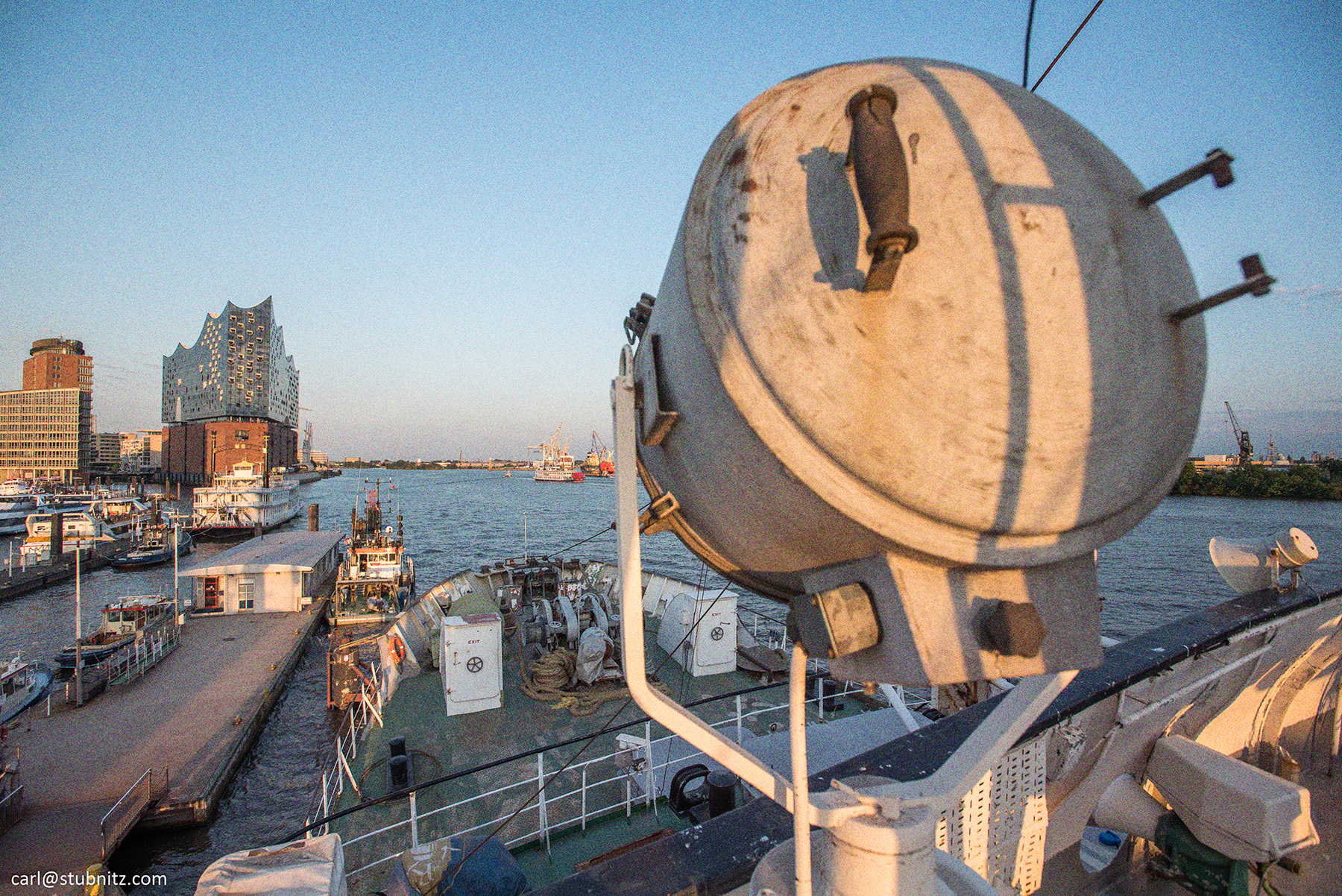 Die Stubnitz an den Landungsbrücken 2019. Im Vordergrund ein Suchscheinwerfer auf dem Deck der Stubnitz. Im Hintergrund die Elbphilharmonie.