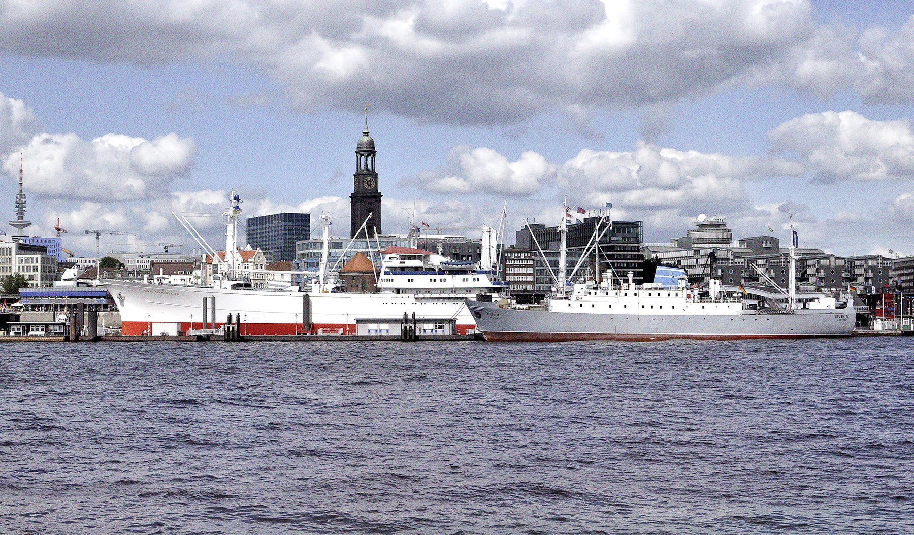 Die Stubnitz an den Hamburger Landungsbrücken. Im Hintegrund weitere Schiffe und Boote sowie die Spitze des Michels.