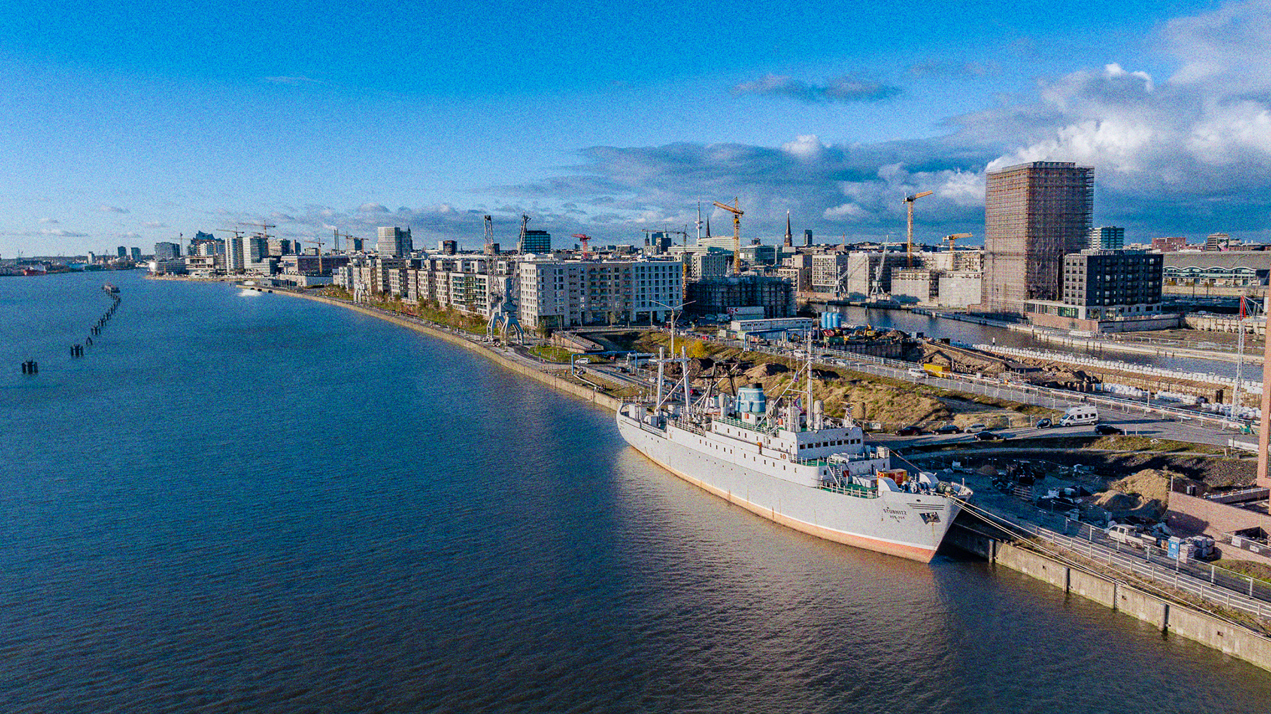 Die Stubnitz an ihrem aktuellen Liegeplatz an den Elbbrücken. Fotografiert aus der Vogelperspektive von schräg vorne. Im Hintergrund die HafenCity und Baukräne, links das Wasser.