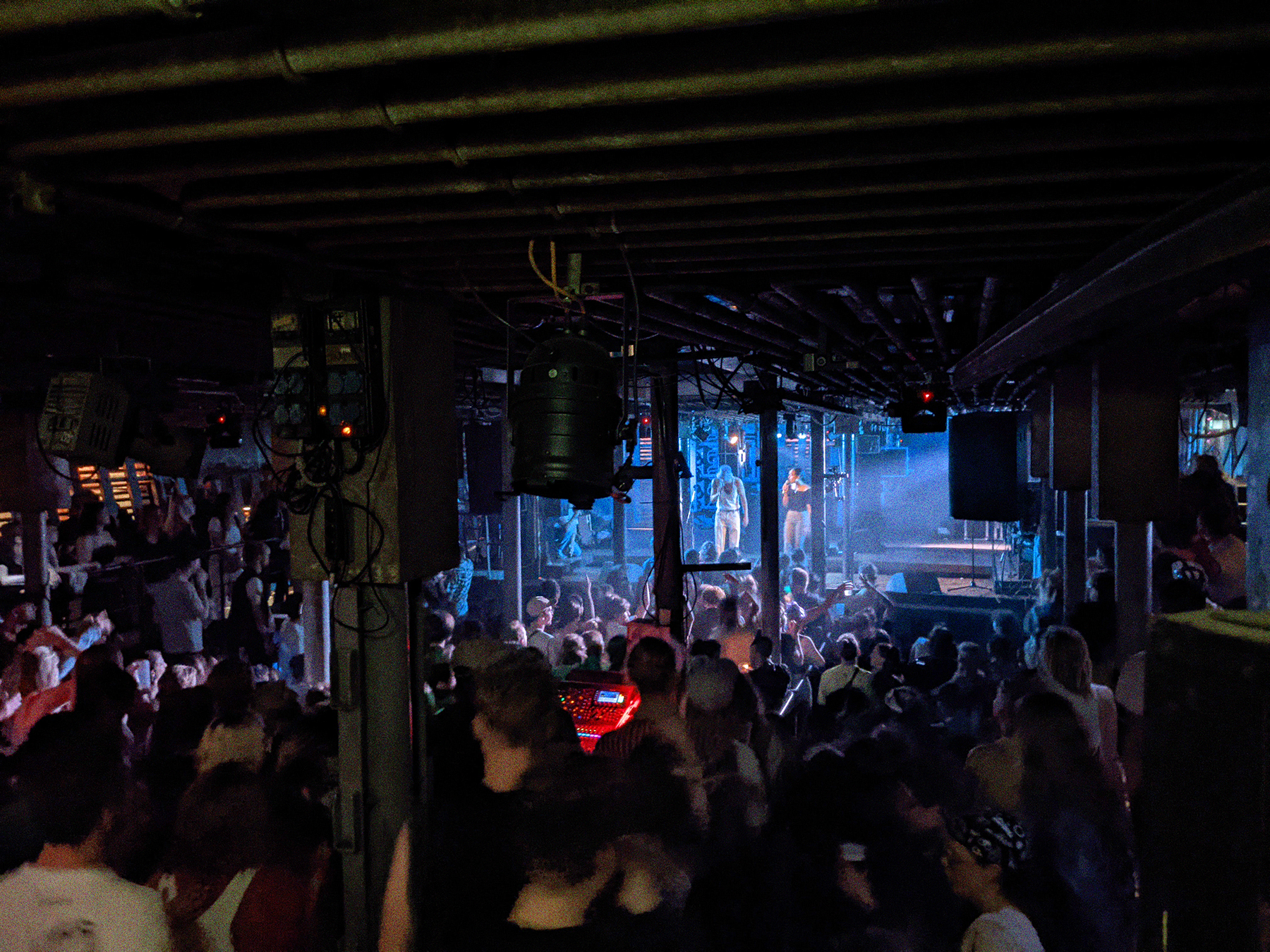 Ein Konzert von Erotik Toy Records in Laderaum 4. Im Vordergrund ein großes tanzendes Publikum. Auf der Bühne in blauem Licht die Musiker:innen.