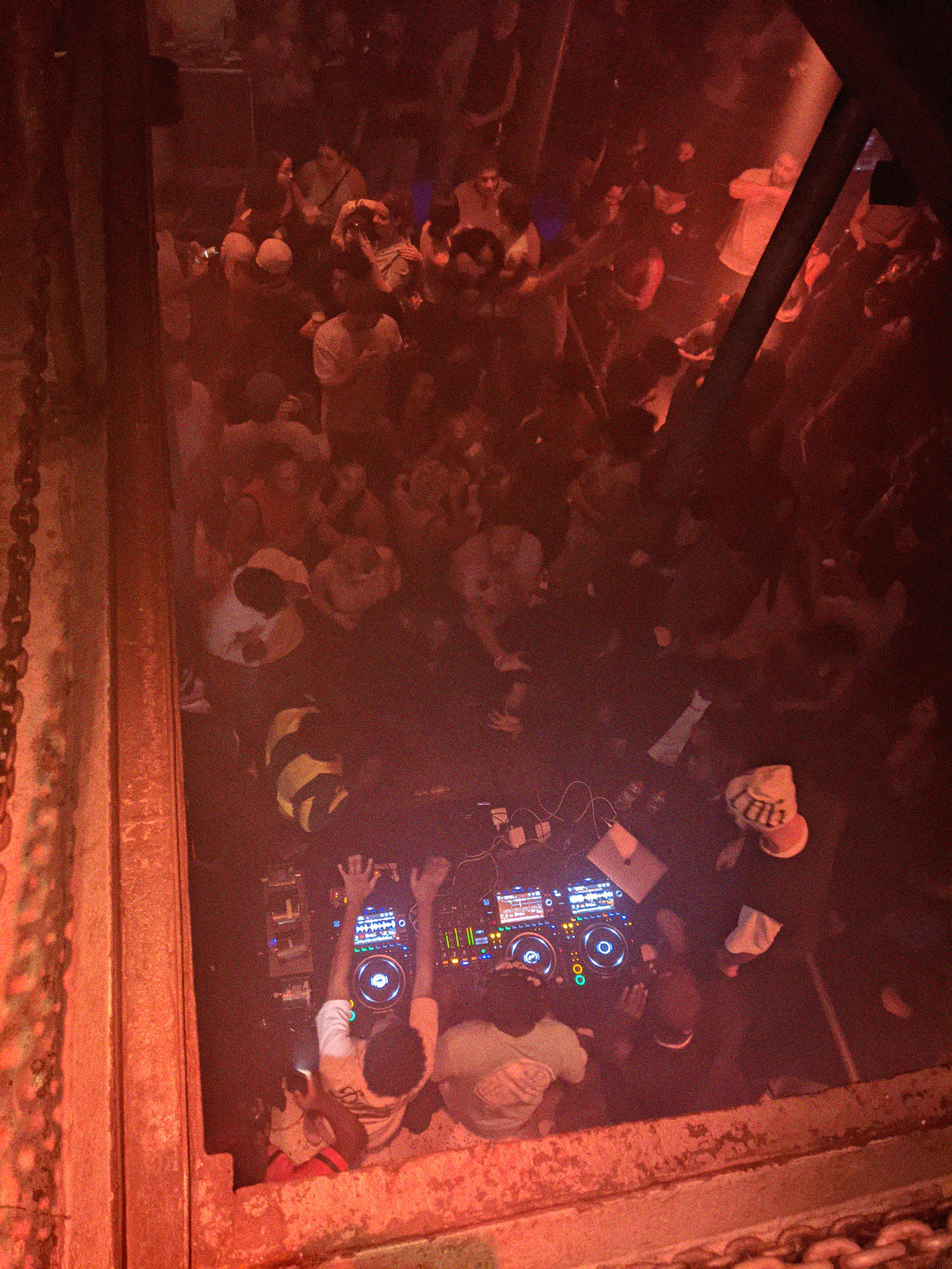 Eine Clubveranstaltung in Laderaum 4, fotografiert aus der Verarbeitung nach unten. Im unteren Teil des Fotos ein DJ-Pult, hinter dem mehrere Menschen stehen. Im oberen Teil des Fotos das feiernde Publikum. Der Raum ist voll.