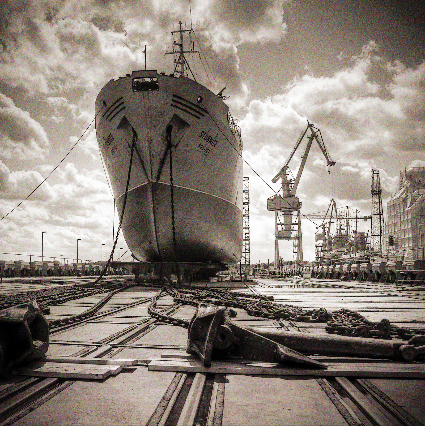 Die Stubnitz im Trockendock in Stralsund 2009. Foto von der Stubnitz von vorne unten. Die Ankerketten liegen ausgebreitet vor dem Schiff. Kräne im Hintergrund.