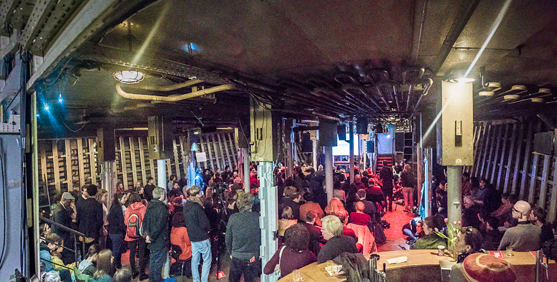 Eine Konferenz in Laderaum 1, fotografiert aus einer Ecke des Raumes. Der Raum ist gefüllt mit Menschen, die zu einer Leinwand im Hintergrund gerichtet sind.